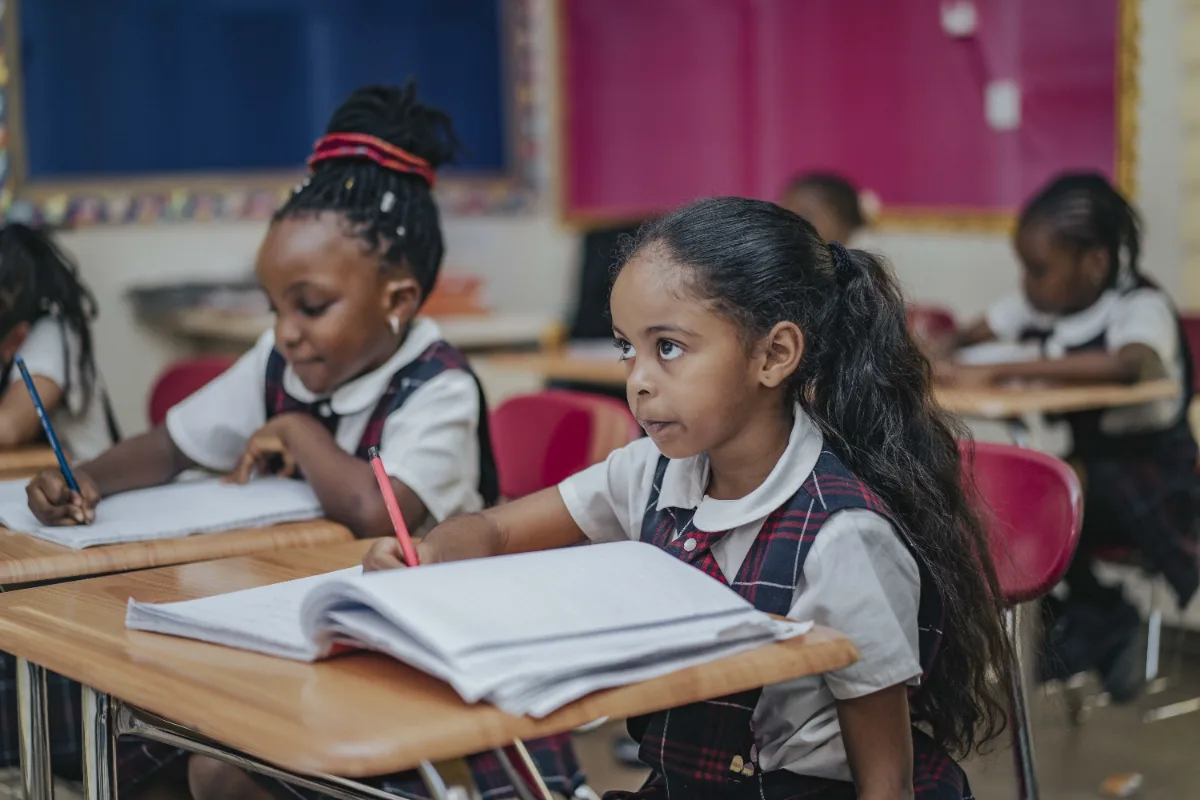 Two students writing in notebooks at their classroom desks.